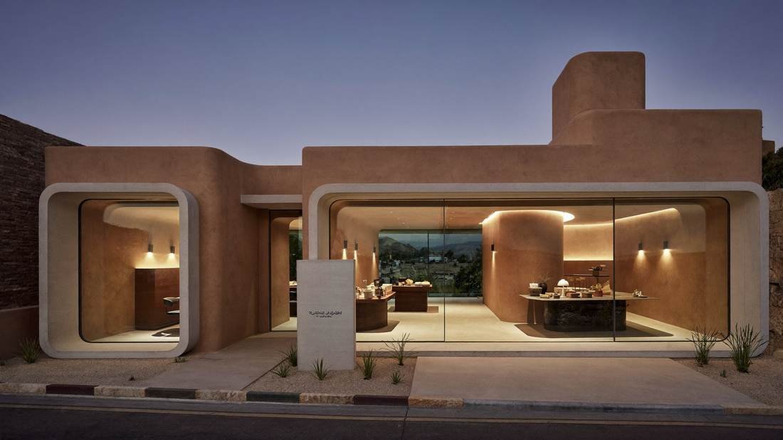 Earth-toned pavilion exterior at dusk, its arched opening framing the lit interior.