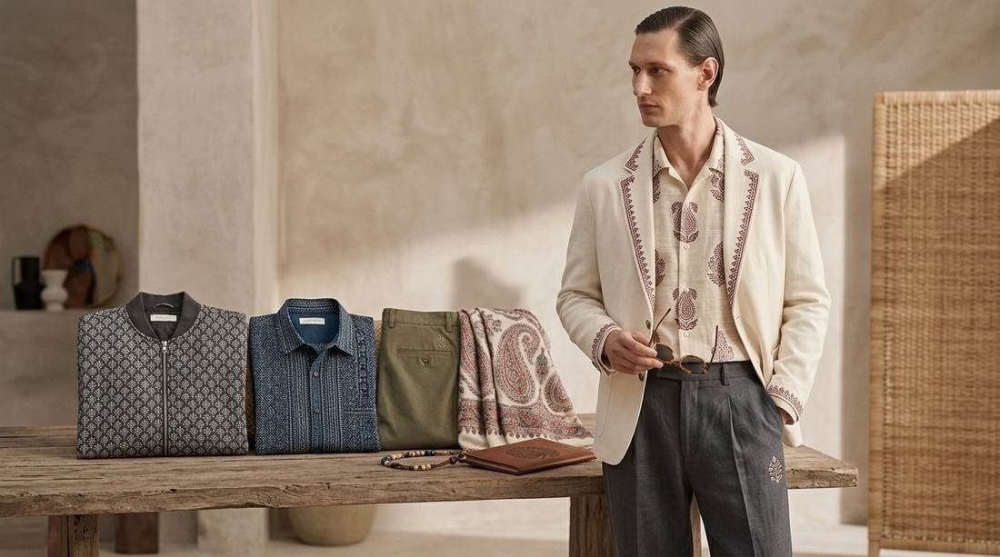 Model in an ivory embroidered shirt beside a rail of indigo block-print shirting and a draped shawl
